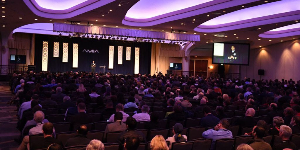 auditorium filled with people in front of a speaker at a podium