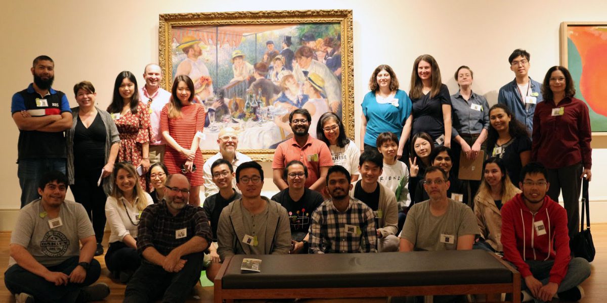 group of people standing and sitting in front of a large painting