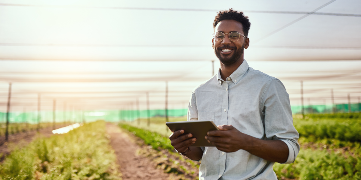 Young African male farmer working on healthy agriculture development strategy on his digital tablet. Smiling field worker outdoors on organic farming and growth sustainability check up
