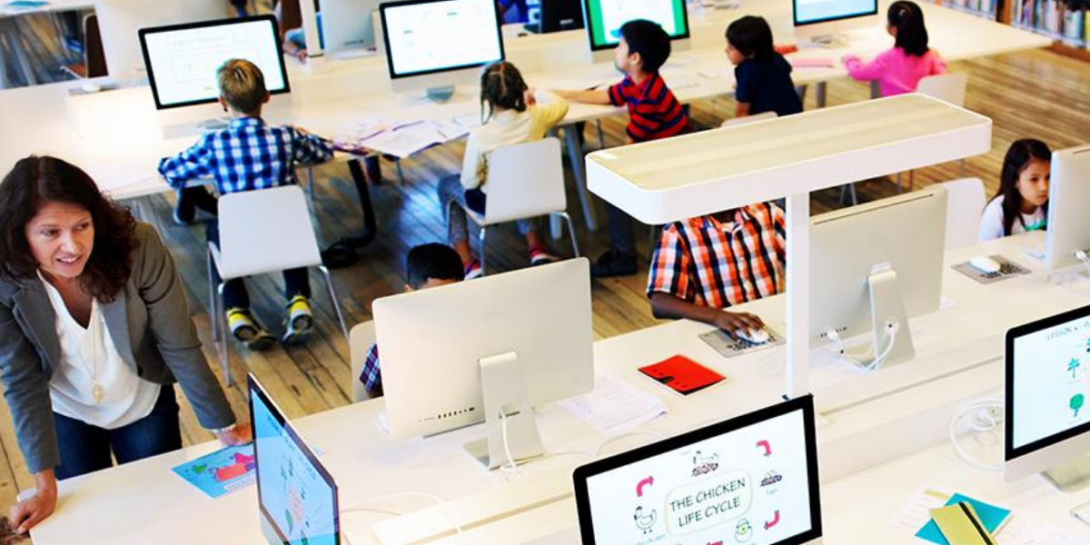 Elementary students in a computer lab with the teacher observing.