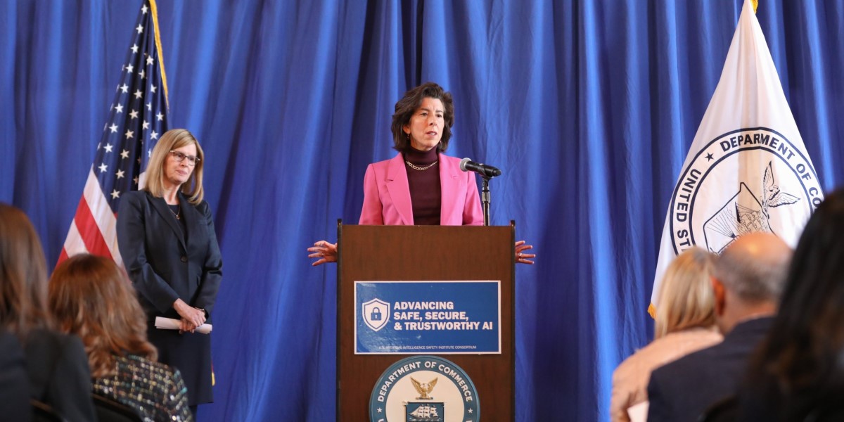 Image of a woman standing behind a podium with the words "advancing safe, secure & trustworthy AI" on the front of it and the Seal of the Department of Commerce.