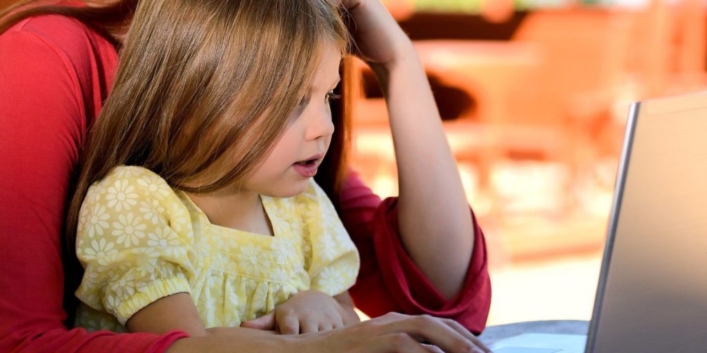 child sitting on person's lap using a laptop