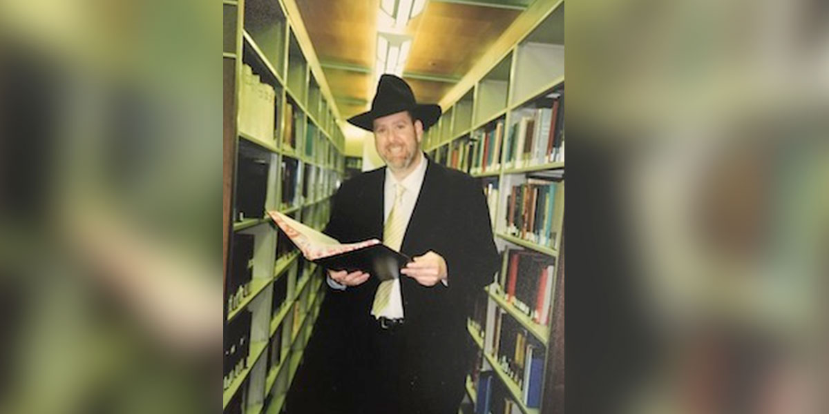 man in between two rows of books, holding a book and smiling