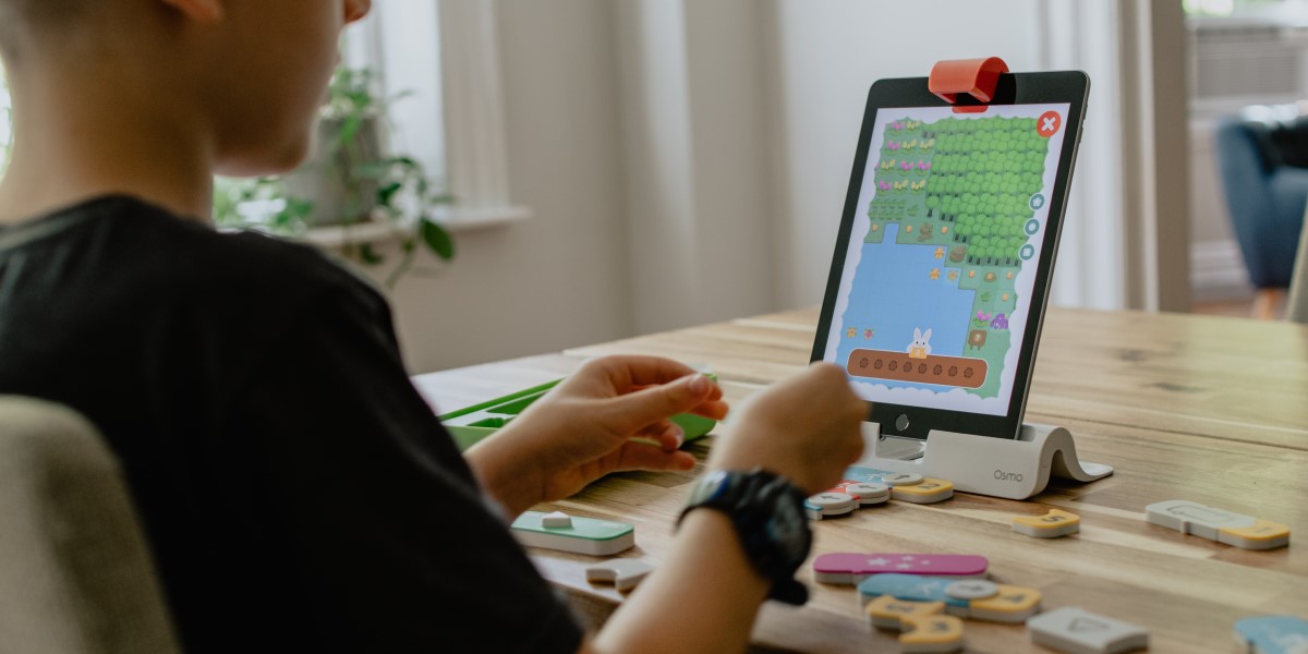 child at a table with an iPad in front of them and block pieces on a table